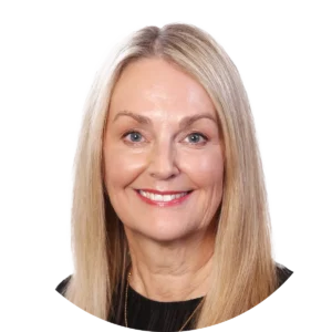 Smiling woman with shoulder-length blonde hair and blue eyes, wearing a black top, against a white background.